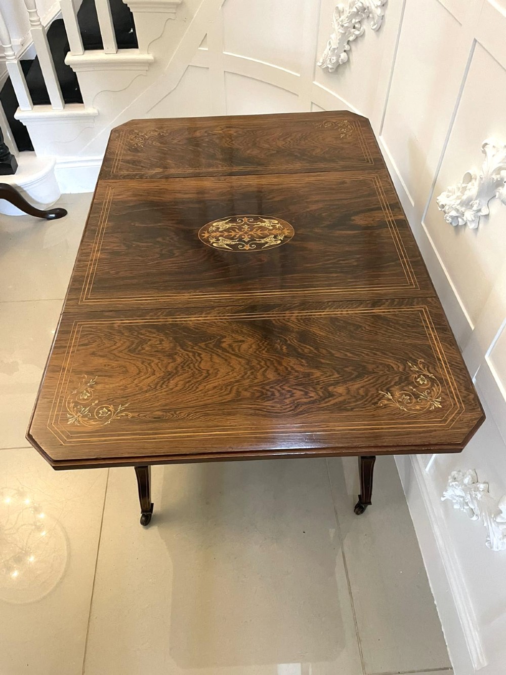 A Victorian rosewood drop-leaf centre table featuring floral marquetry inlay, turned legs on brass castors, and a lower tiered shelf with a spindle gallery. View VIII