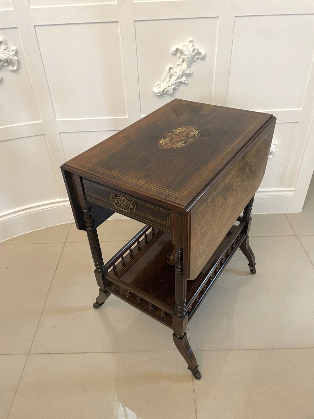 A Victorian rosewood drop-leaf centre table featuring floral marquetry inlay, turned legs on brass castors, and a lower tiered shelf with a spindle gallery. View IX