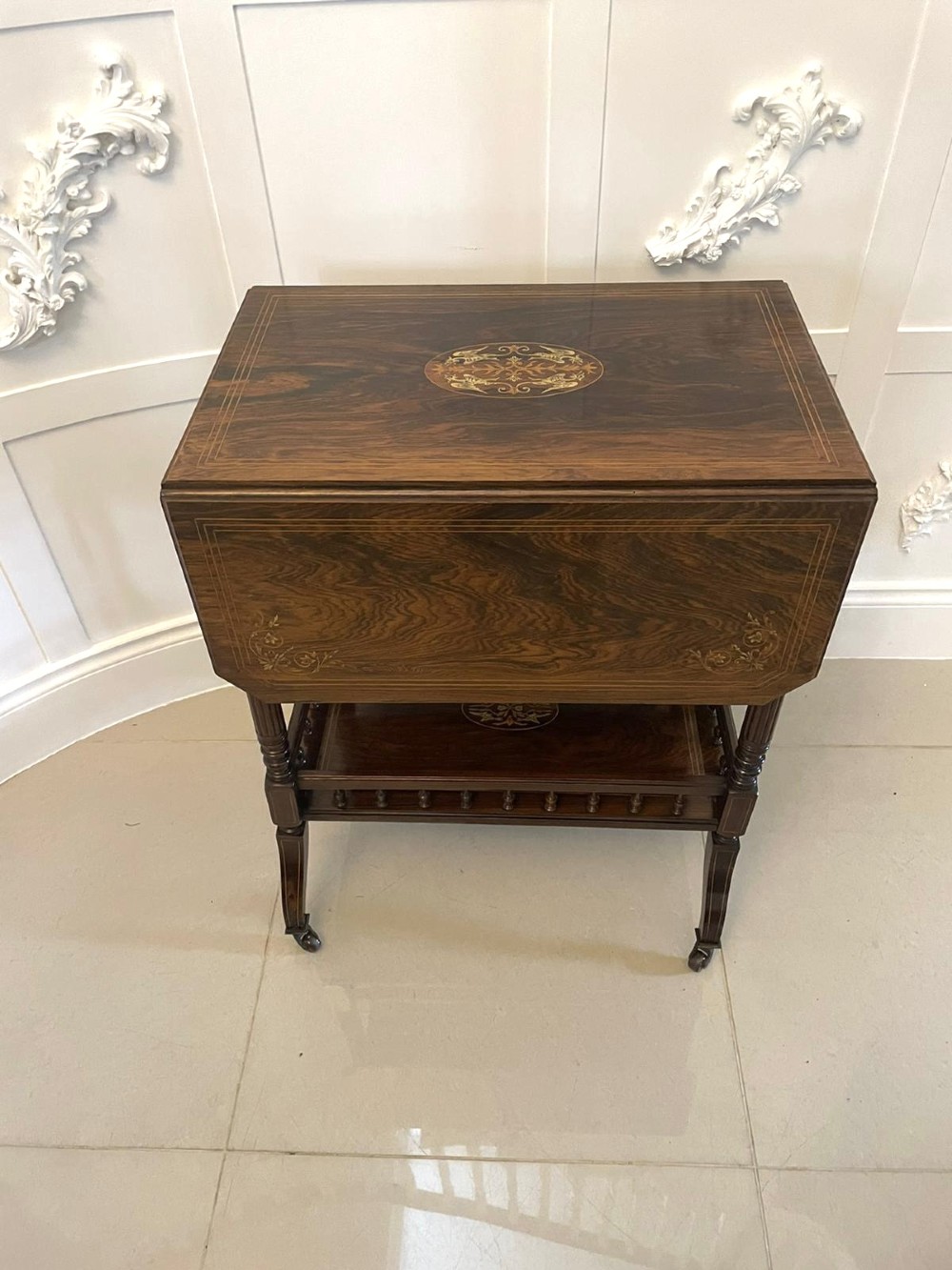 A Victorian rosewood drop-leaf centre table featuring floral marquetry inlay, turned legs on brass castors, and a lower tiered shelf with a spindle gallery. View XV