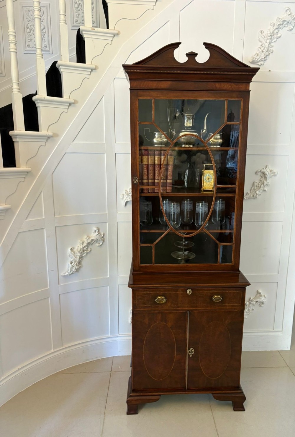 A tall Victorian mahogany glazed bookcase featuring a swan-neck pediment, geometric astragal glazing, an inlaid drawer, and a lower two-door cupboard. View IV