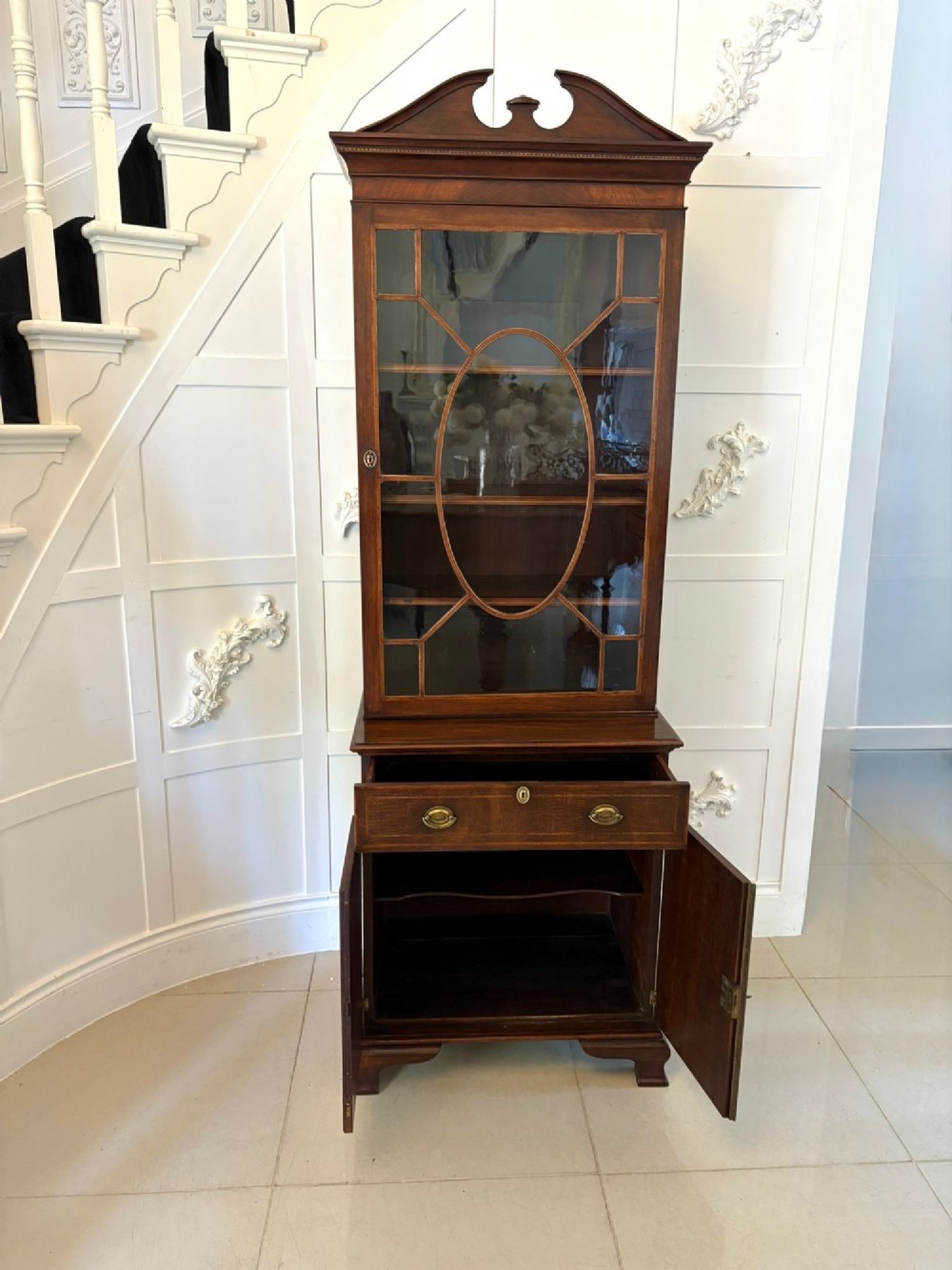 A tall Victorian mahogany glazed bookcase featuring a swan-neck pediment, geometric astragal glazing, an inlaid drawer, and a lower two-door cupboard. View VII
