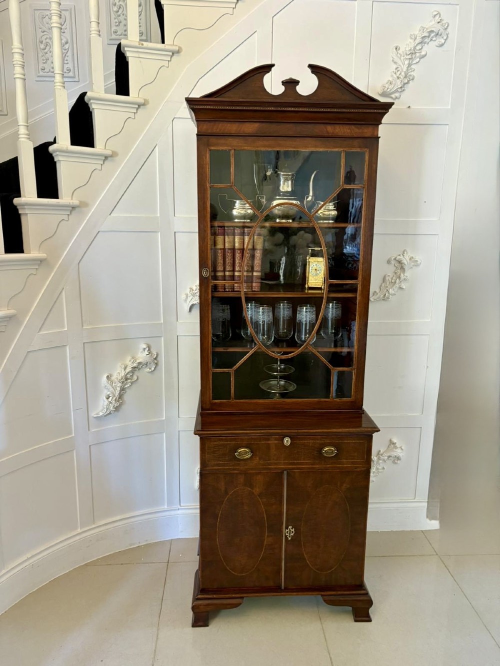 A tall Victorian mahogany glazed bookcase featuring a swan-neck pediment, geometric astragal glazing, an inlaid drawer, and a lower two-door cupboard. View XV