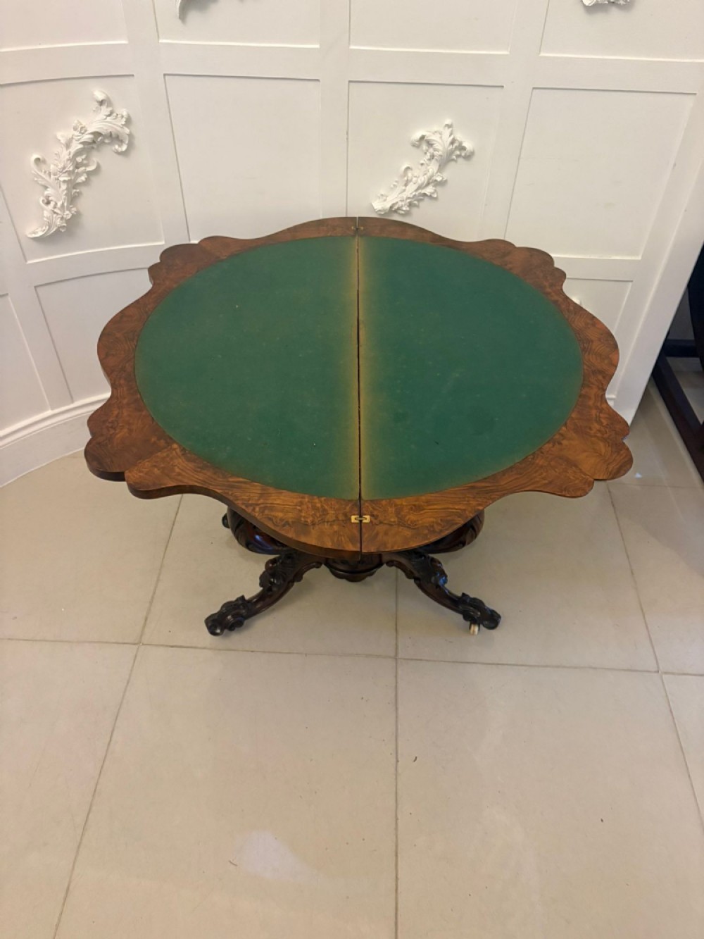 A Victorian burr walnut card table featuring a serpentine-shaped fold-over top set upon a carved pedestal base with four scroll feet on castors. View IV
