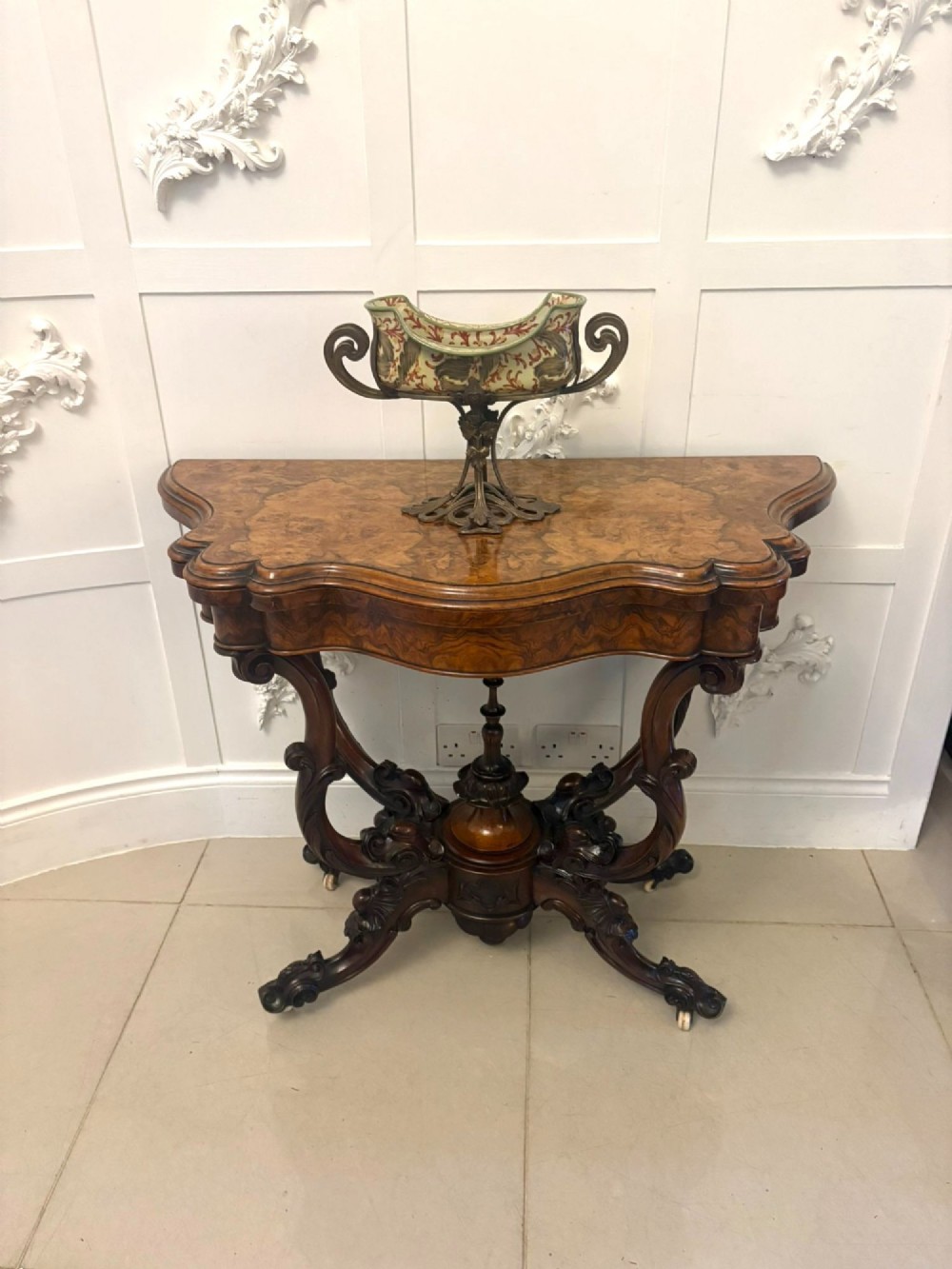 A Victorian burr walnut card table featuring a serpentine-shaped fold-over top set upon a carved pedestal base with four scroll feet on castors. View VI