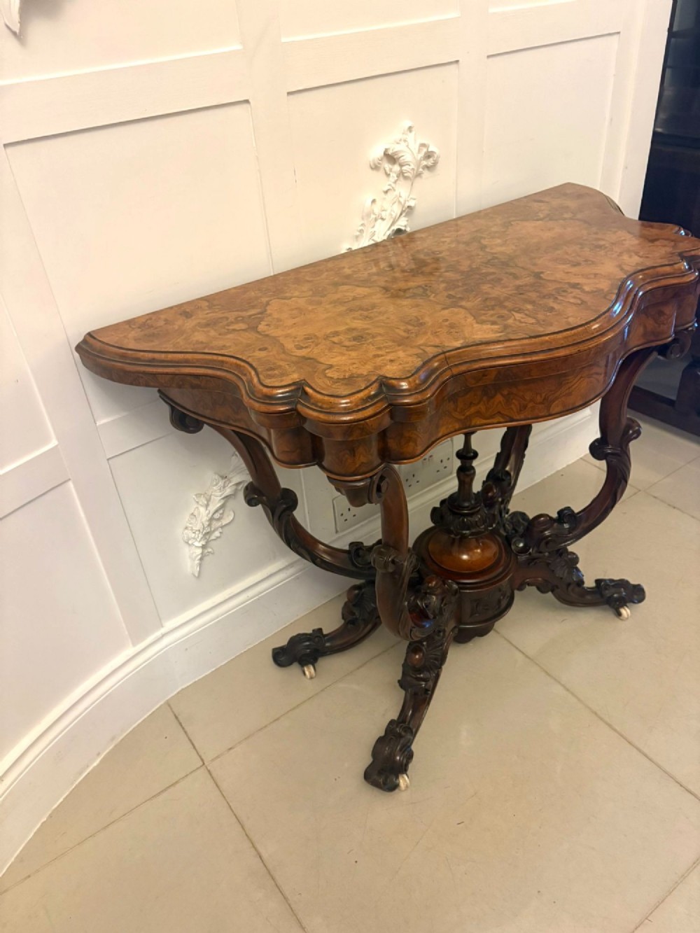 A Victorian burr walnut card table featuring a serpentine-shaped fold-over top set upon a carved pedestal base with four scroll feet on castors. View VII
