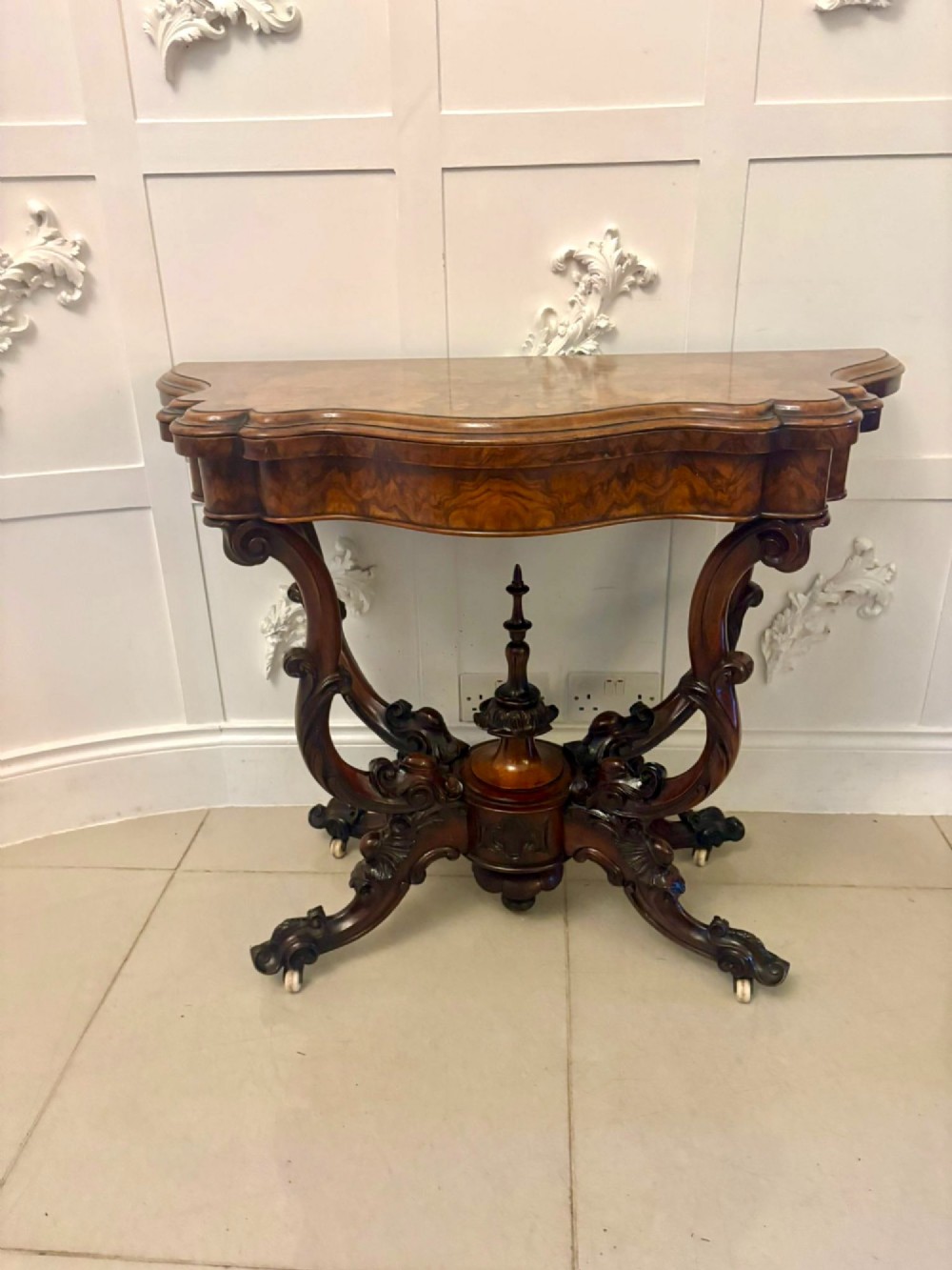A Victorian burr walnut card table featuring a serpentine-shaped fold-over top set upon a carved pedestal base with four scroll feet on castors. View XIII