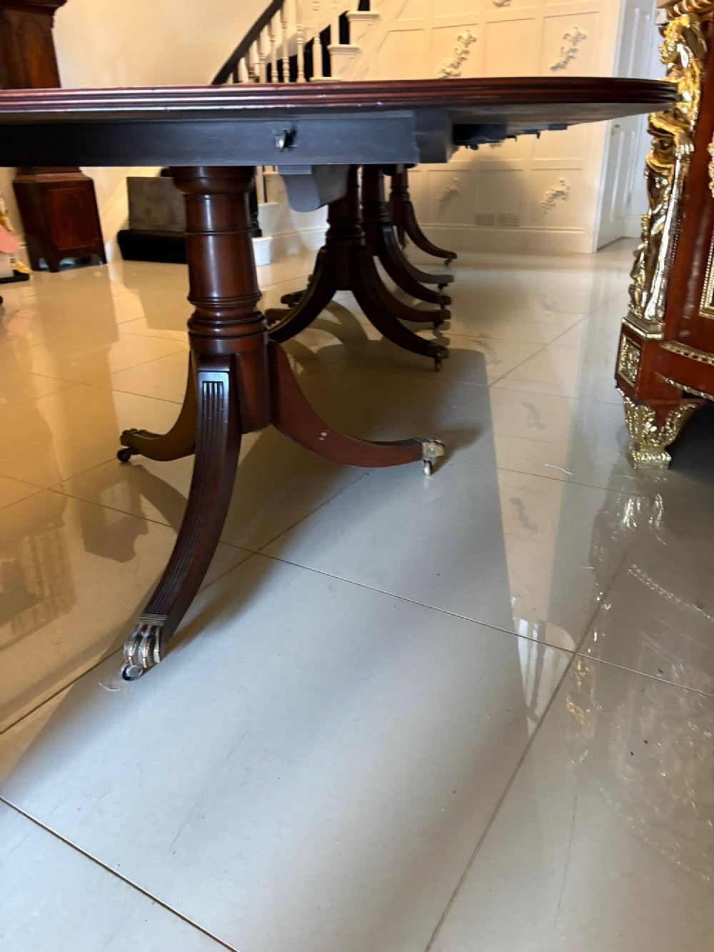 An exceptionally long mahogany banquet dining table supported on four turned pedestals with splayed legs and brass castors. View V