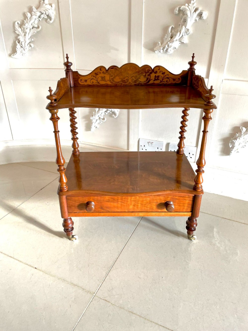 An antique Victorian burr walnut two-tier lamp table featuring a decorative floral inlaid gallery, turned finials, spiral columns, a single drawer, and brass castors. View IV