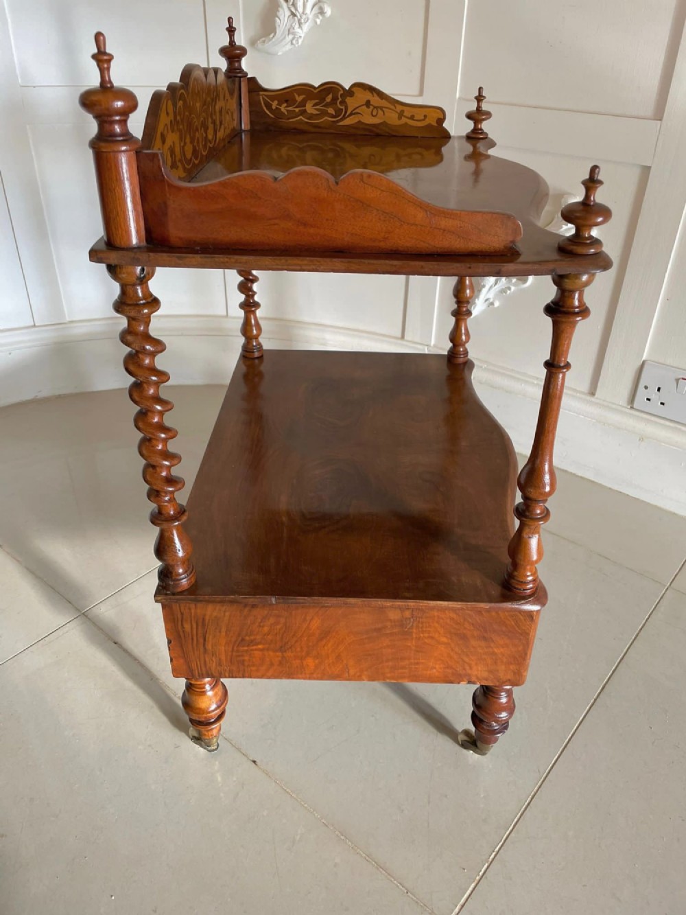An antique Victorian burr walnut two-tier lamp table featuring a decorative floral inlaid gallery, turned finials, spiral columns, a single drawer, and brass castors. View V