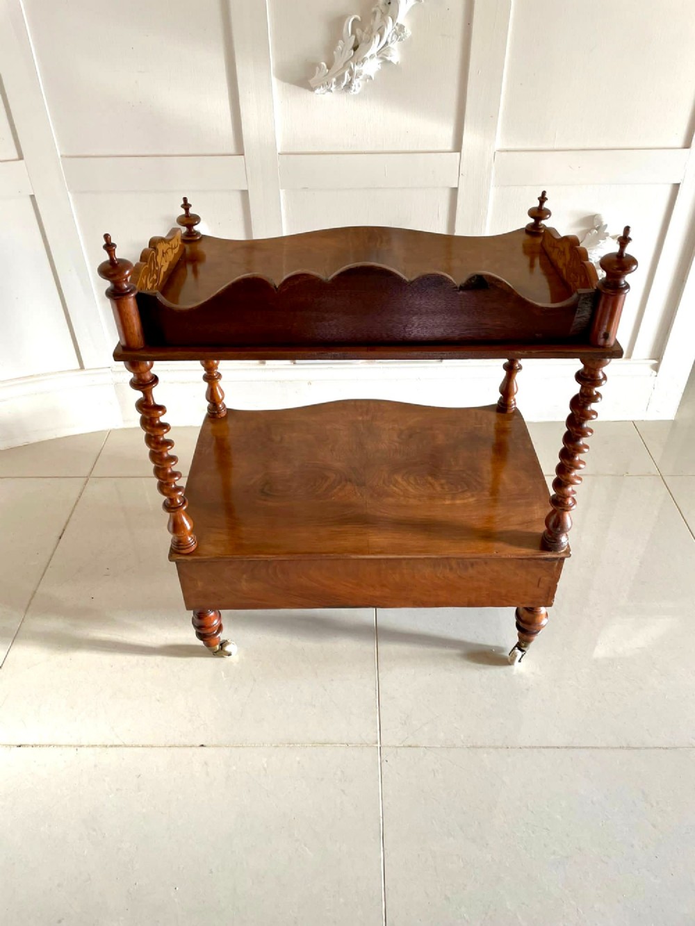 An antique Victorian burr walnut two-tier lamp table featuring a decorative floral inlaid gallery, turned finials, spiral columns, a single drawer, and brass castors. View IX