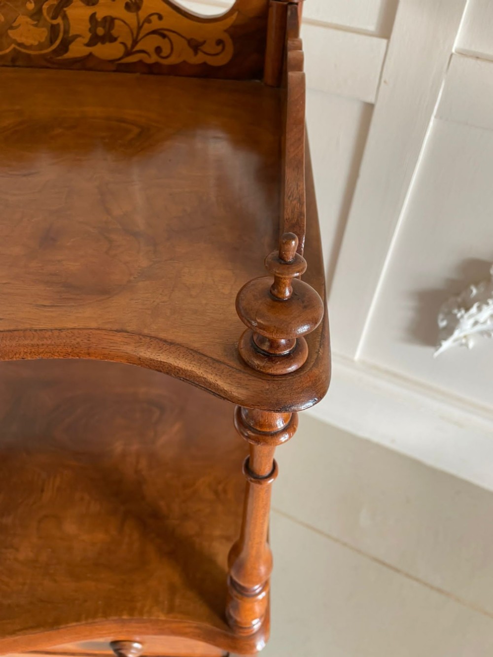 An antique Victorian burr walnut two-tier lamp table featuring a decorative floral inlaid gallery, turned finials, spiral columns, a single drawer, and brass castors. View XV