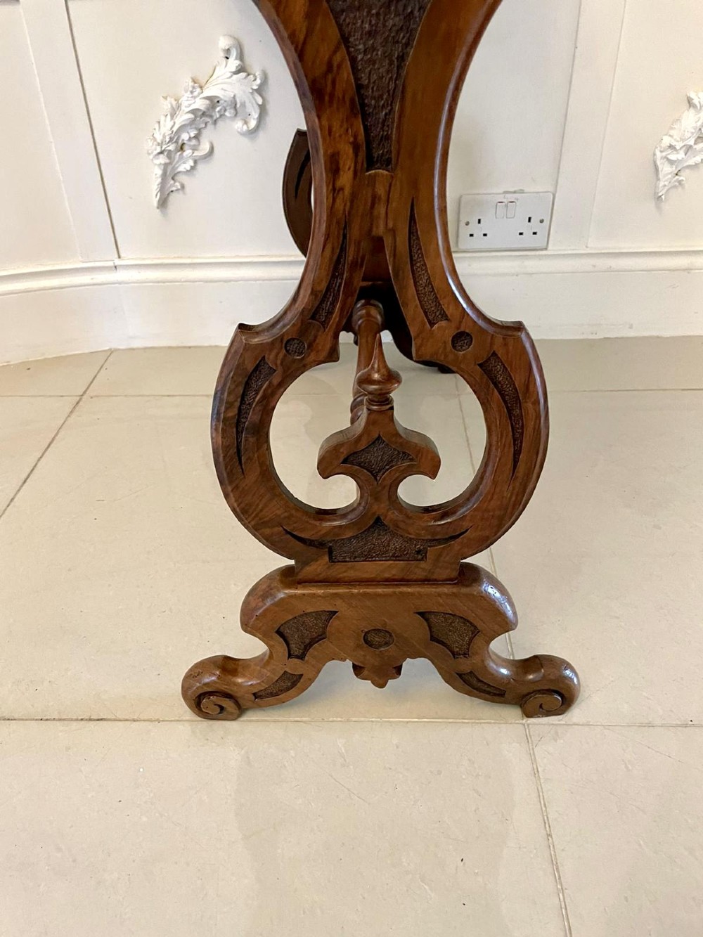 A Victorian burr walnut centre table with a serpentine shaped top, resting on carved pierced end supports and connected by a turned stretcher. View V