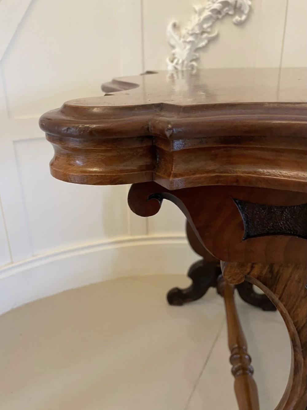 A Victorian burr walnut centre table with a serpentine shaped top, resting on carved pierced end supports and connected by a turned stretcher. View VII