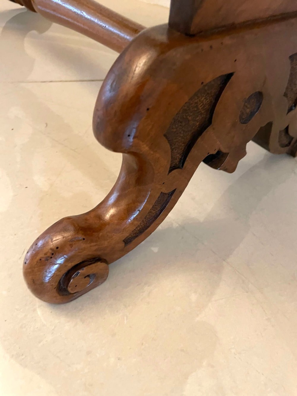 A Victorian burr walnut centre table with a serpentine shaped top, resting on carved pierced end supports and connected by a turned stretcher. View X