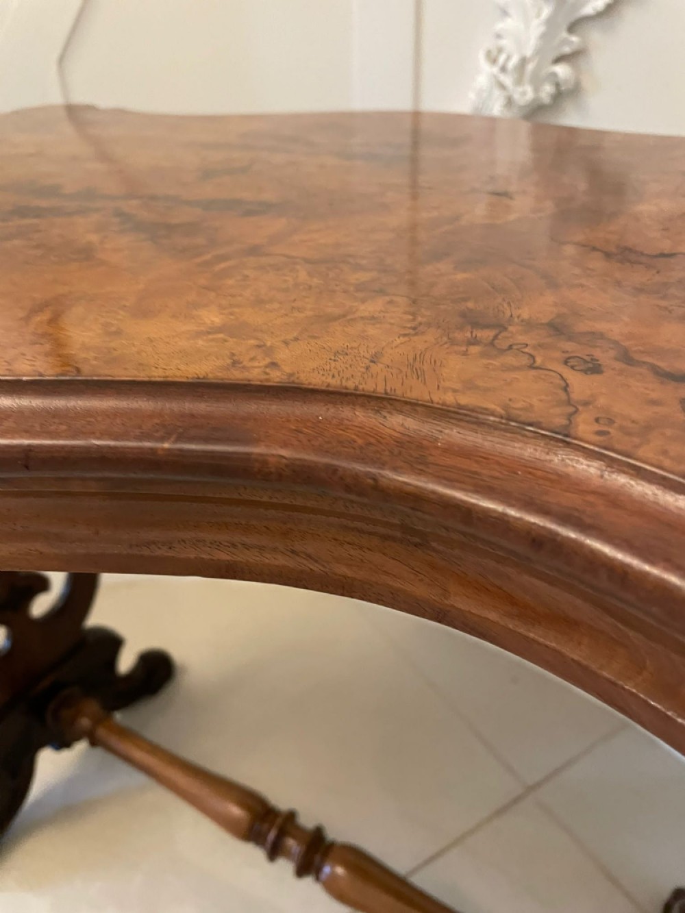 A Victorian burr walnut centre table with a serpentine shaped top, resting on carved pierced end supports and connected by a turned stretcher. View XIV