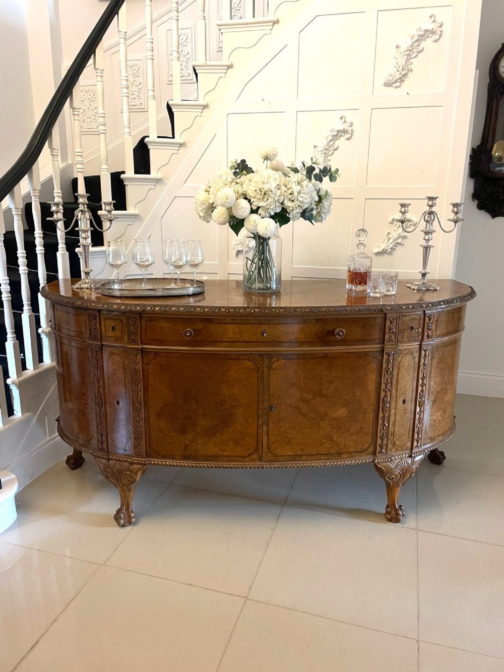 A large burr walnut bow-fronted sideboard featuring carved decorative stiles, central drawers, cupboards, and cabriole legs. View III