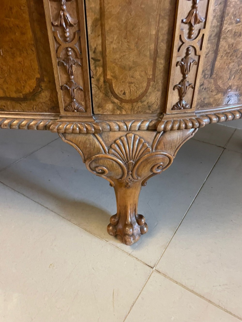 A large burr walnut bow-fronted sideboard featuring carved decorative stiles, central drawers, cupboards, and cabriole legs. View IV