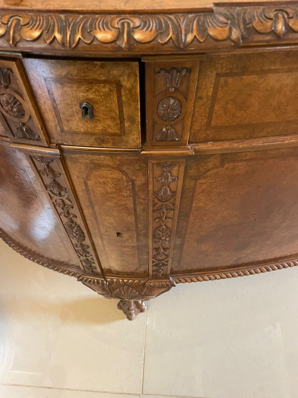A large burr walnut bow-fronted sideboard featuring carved decorative stiles, central drawers, cupboards, and cabriole legs. View V