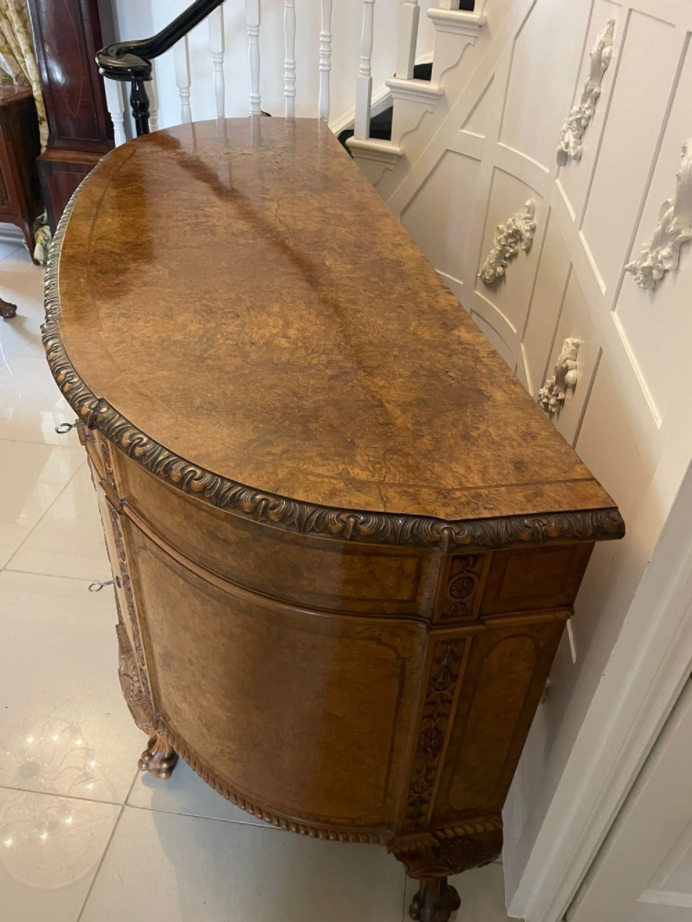 A large burr walnut bow-fronted sideboard featuring carved decorative stiles, central drawers, cupboards, and cabriole legs. View VII