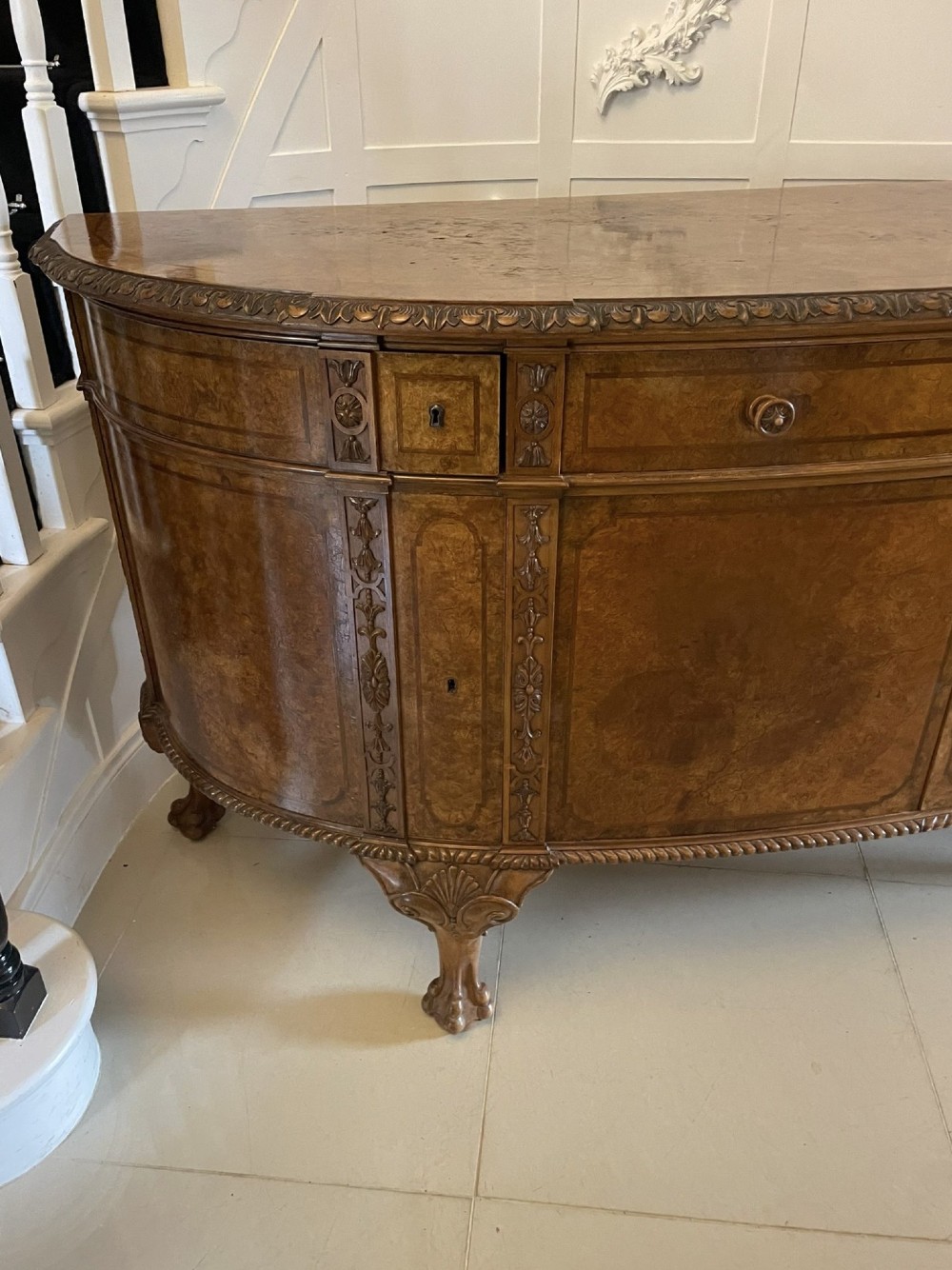 A large burr walnut bow-fronted sideboard featuring carved decorative stiles, central drawers, cupboards, and cabriole legs. View XI
