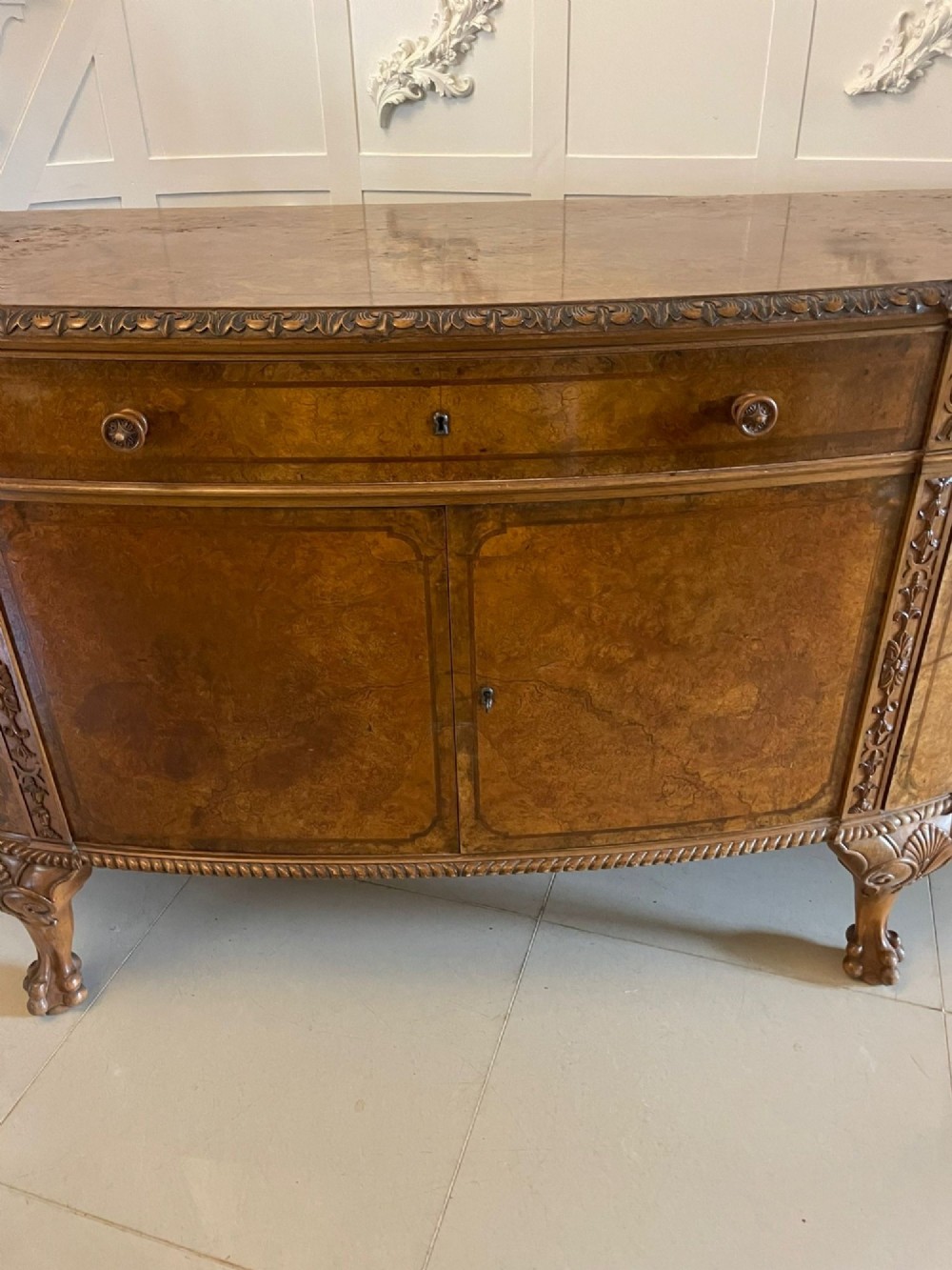 A large burr walnut bow-fronted sideboard featuring carved decorative stiles, central drawers, cupboards, and cabriole legs. View XII
