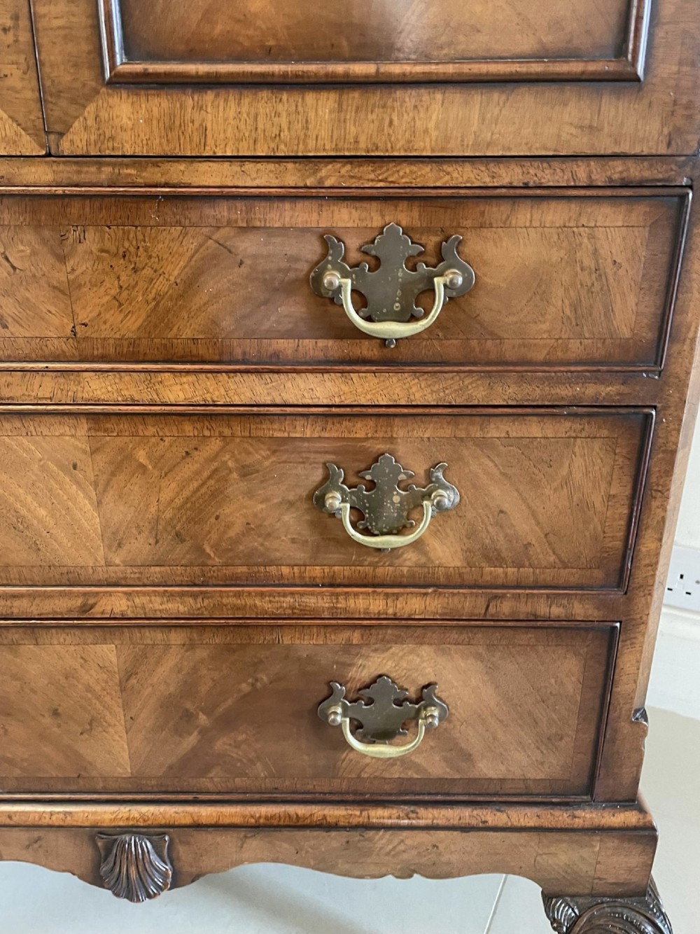 An antique burr walnut chest on stand featuring a two-door cupboard with arched panels above three long drawers, resting on carved cabriole legs. View V