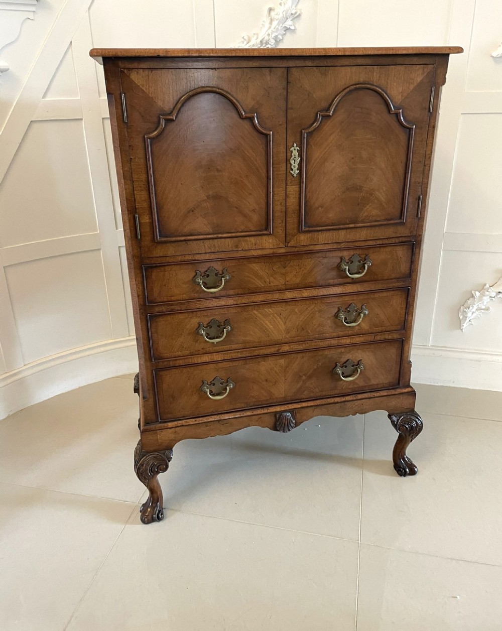 An antique burr walnut chest on stand featuring a two-door cupboard with arched panels above three long drawers, resting on carved cabriole legs. View XII