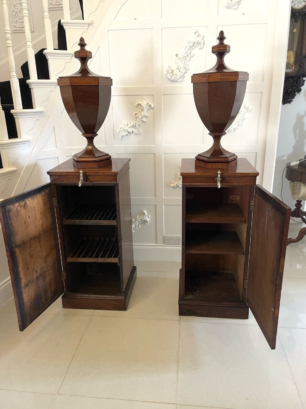 A pair of George III mahogany wine urns featuring flame mahogany oval inlay panels resting atop matching square pedestal cupboards with brass spigots. View III
