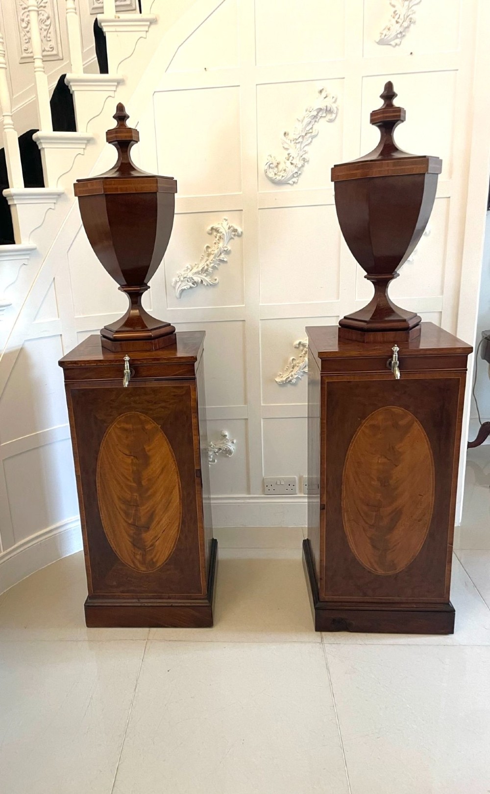 A pair of George III mahogany wine urns featuring flame mahogany oval inlay panels resting atop matching square pedestal cupboards with brass spigots. View XV