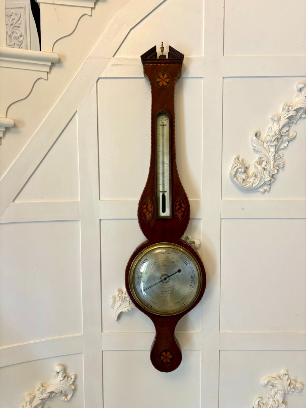 An antique George III mahogany banjo wall barometer featuring shell marquetry inlays, a silvered circular dial, an integrated mercury thermometer, and a broken-arch pediment with a brass finial.