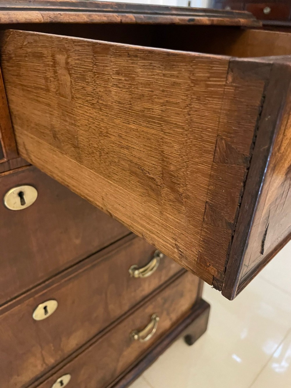 A George I period chest of drawers in figured walnut featuring two short drawers over three long drawers with brass drop handles and bracket feet. View II
