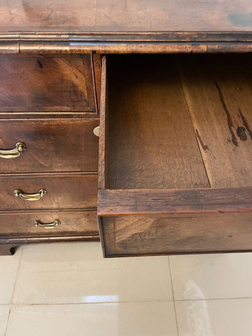 A George I period chest of drawers in figured walnut featuring two short drawers over three long drawers with brass drop handles and bracket feet. View III