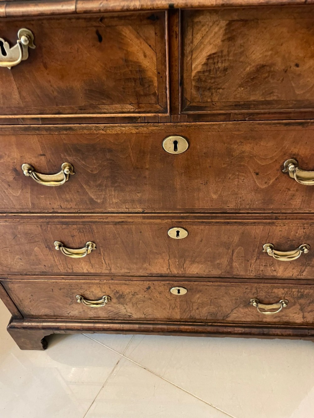 A George I period chest of drawers in figured walnut featuring two short drawers over three long drawers with brass drop handles and bracket feet. View IV