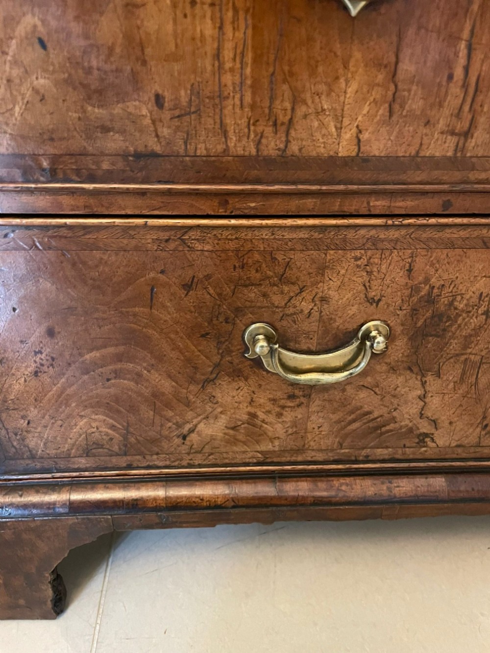 A George I period chest of drawers in figured walnut featuring two short drawers over three long drawers with brass drop handles and bracket feet. View VI