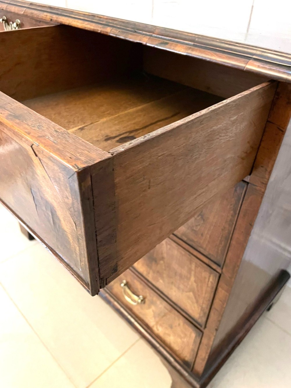 A George I period chest of drawers in figured walnut featuring two short drawers over three long drawers with brass drop handles and bracket feet. View IX