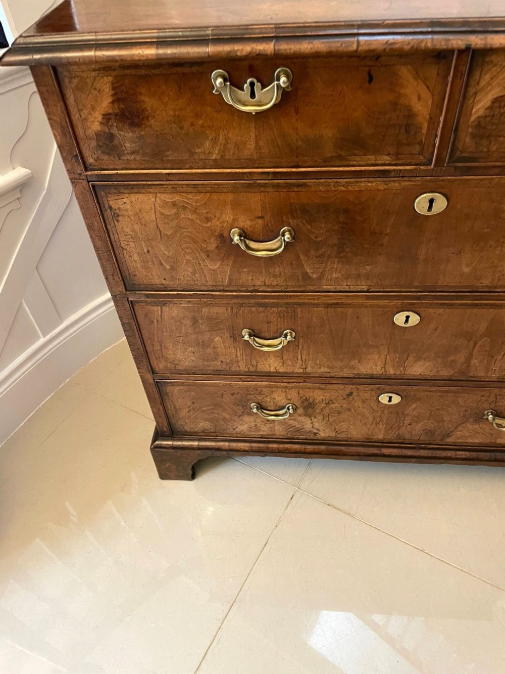 A George I period chest of drawers in figured walnut featuring two short drawers over three long drawers with brass drop handles and bracket feet. View XII