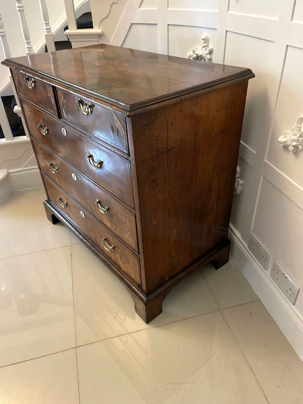 A George I period chest of drawers in figured walnut featuring two short drawers over three long drawers with brass drop handles and bracket feet. View XIII