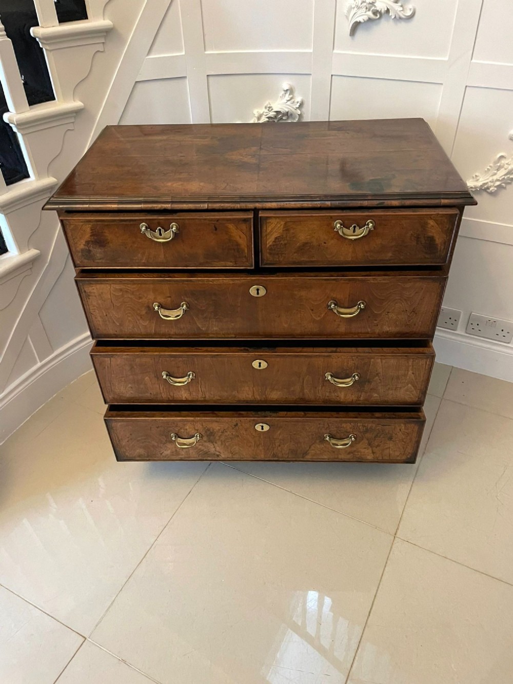 A George I period chest of drawers in figured walnut featuring two short drawers over three long drawers with brass drop handles and bracket feet. View XIV