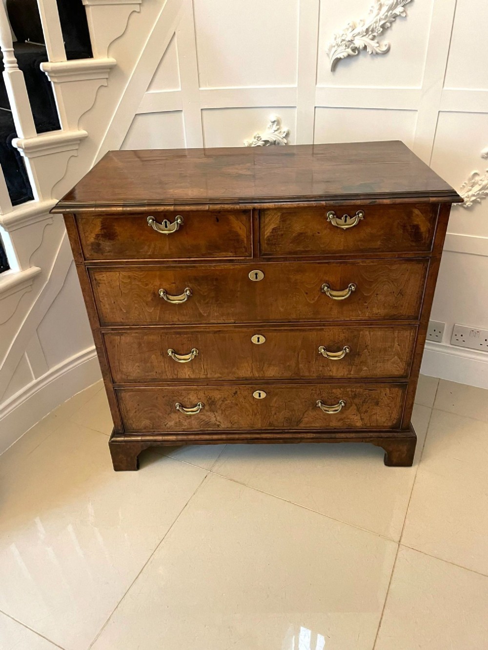 A George I period chest of drawers in figured walnut featuring two short drawers over three long drawers with brass drop handles and bracket feet. View XV