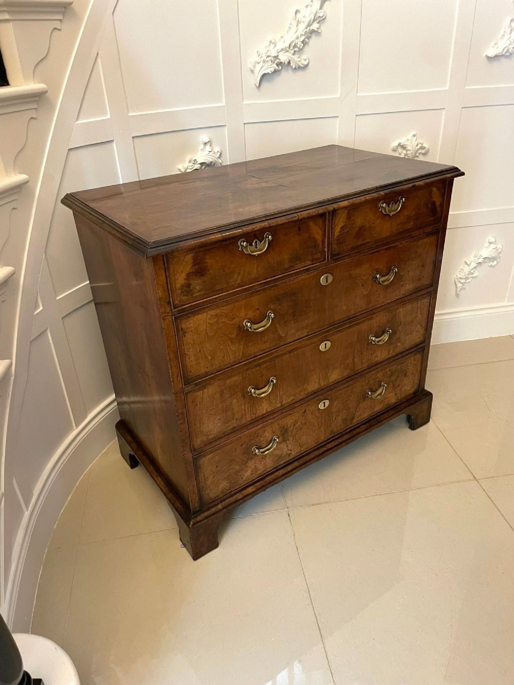 A George I period chest of drawers in figured walnut featuring two short drawers over three long drawers with brass drop handles and bracket feet.