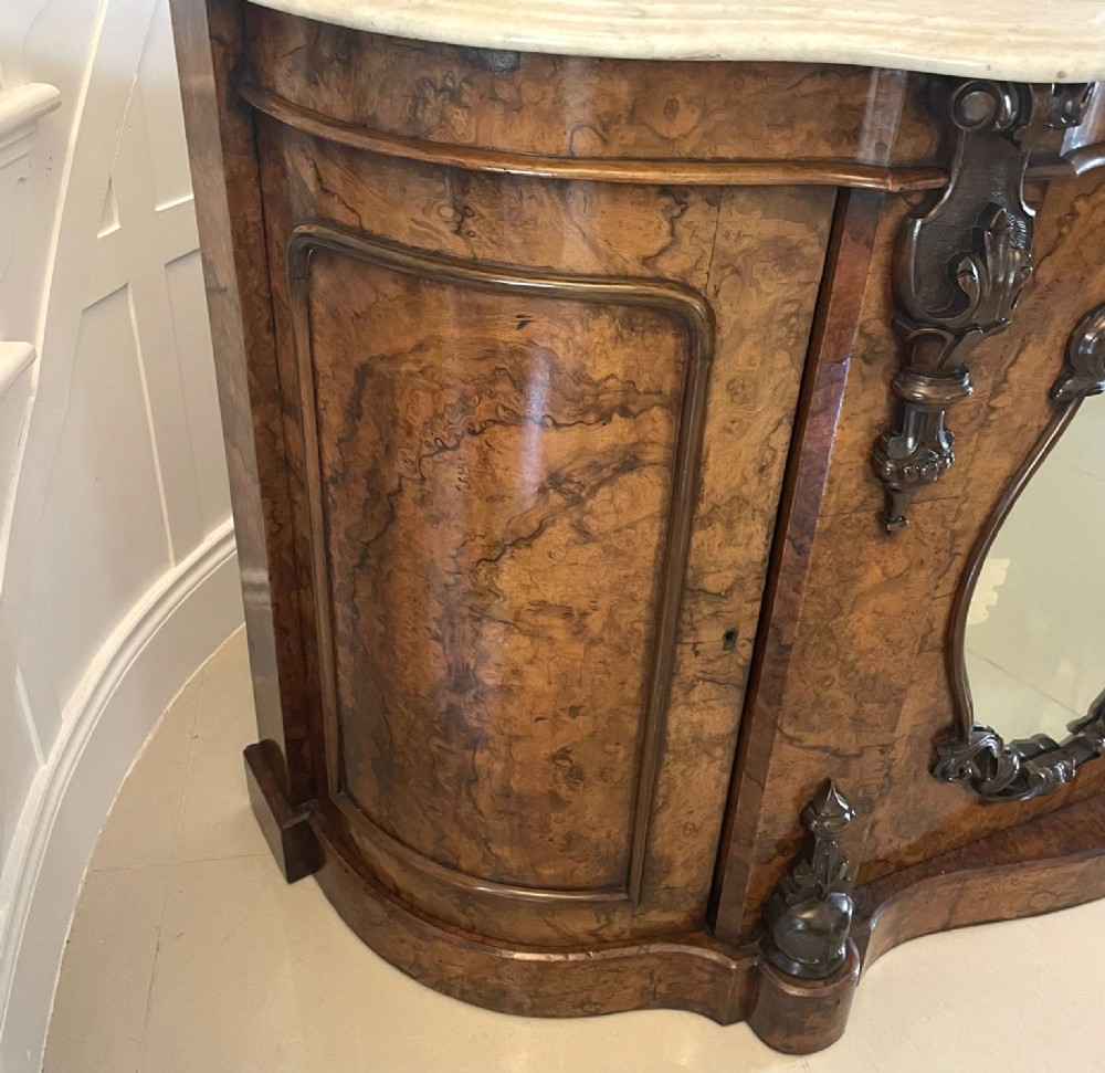 A Victorian burr walnut credenza featuring a serpentine white marble top, mirrored cupboard doors, and a large oval mirror back with carved scrolling detail. View II