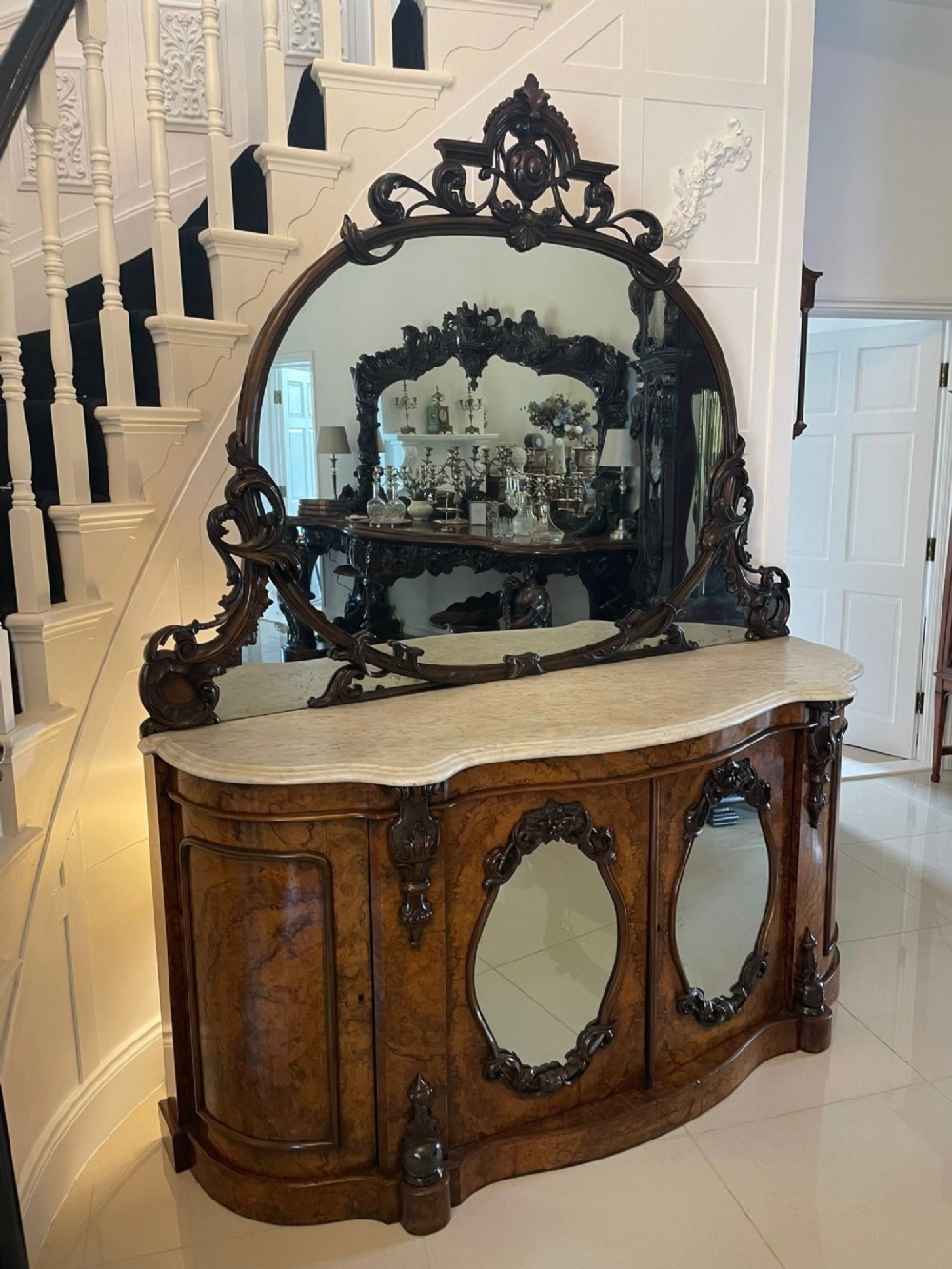 A Victorian burr walnut credenza featuring a serpentine white marble top, mirrored cupboard doors, and a large oval mirror back with carved scrolling detail. View III