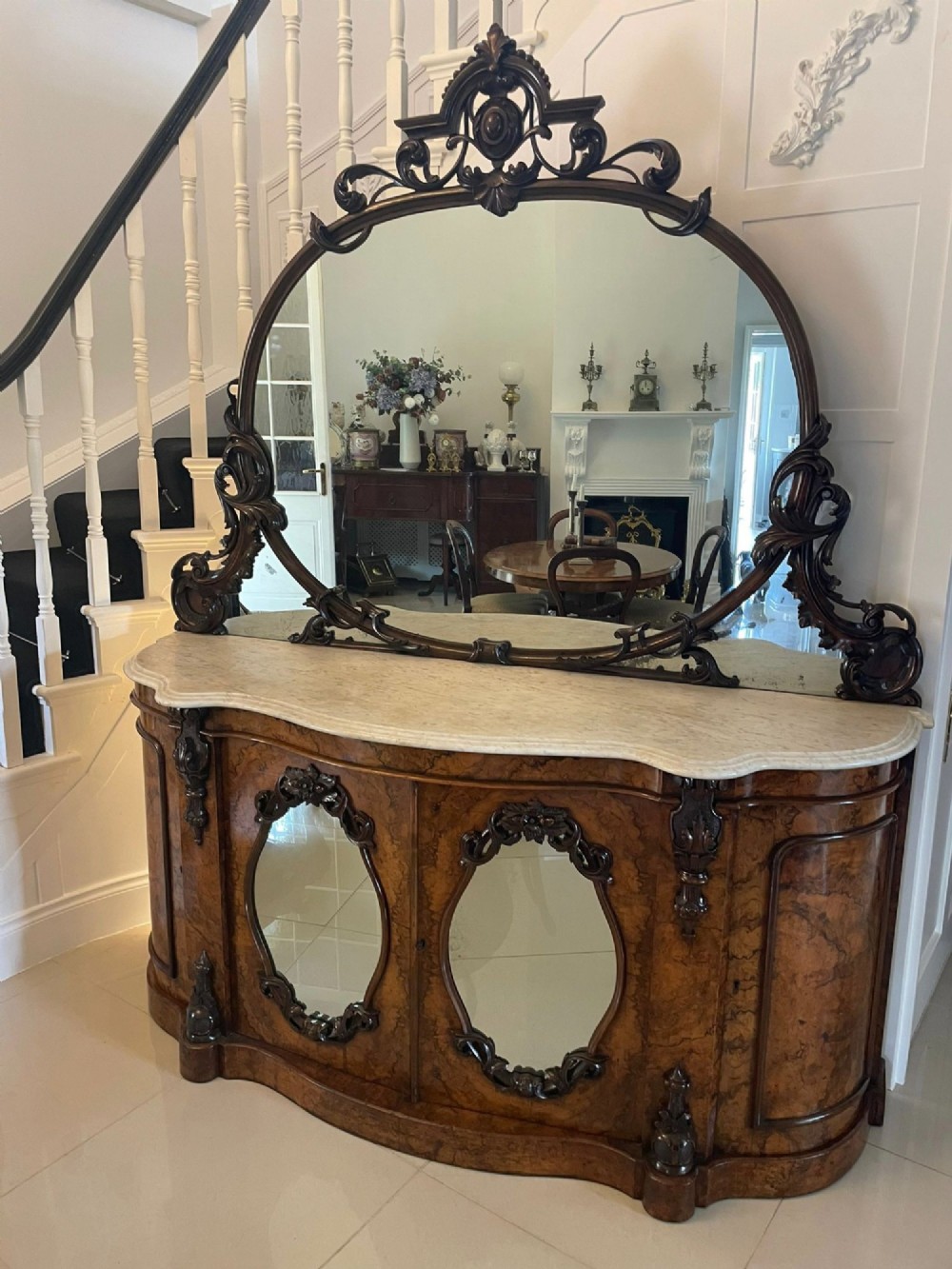 A Victorian burr walnut credenza featuring a serpentine white marble top, mirrored cupboard doors, and a large oval mirror back with carved scrolling detail.