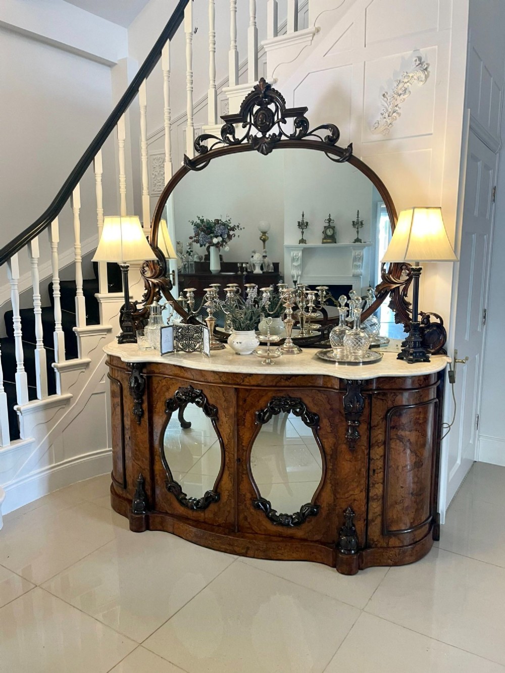 A Victorian burr walnut credenza featuring a serpentine white marble top, mirrored cupboard doors, and a large oval mirror back with carved scrolling detail. View X