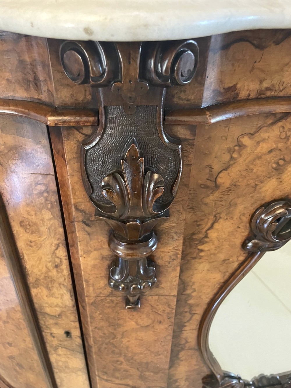 A Victorian burr walnut credenza featuring a serpentine white marble top, mirrored cupboard doors, and a large oval mirror back with carved scrolling detail. View XI