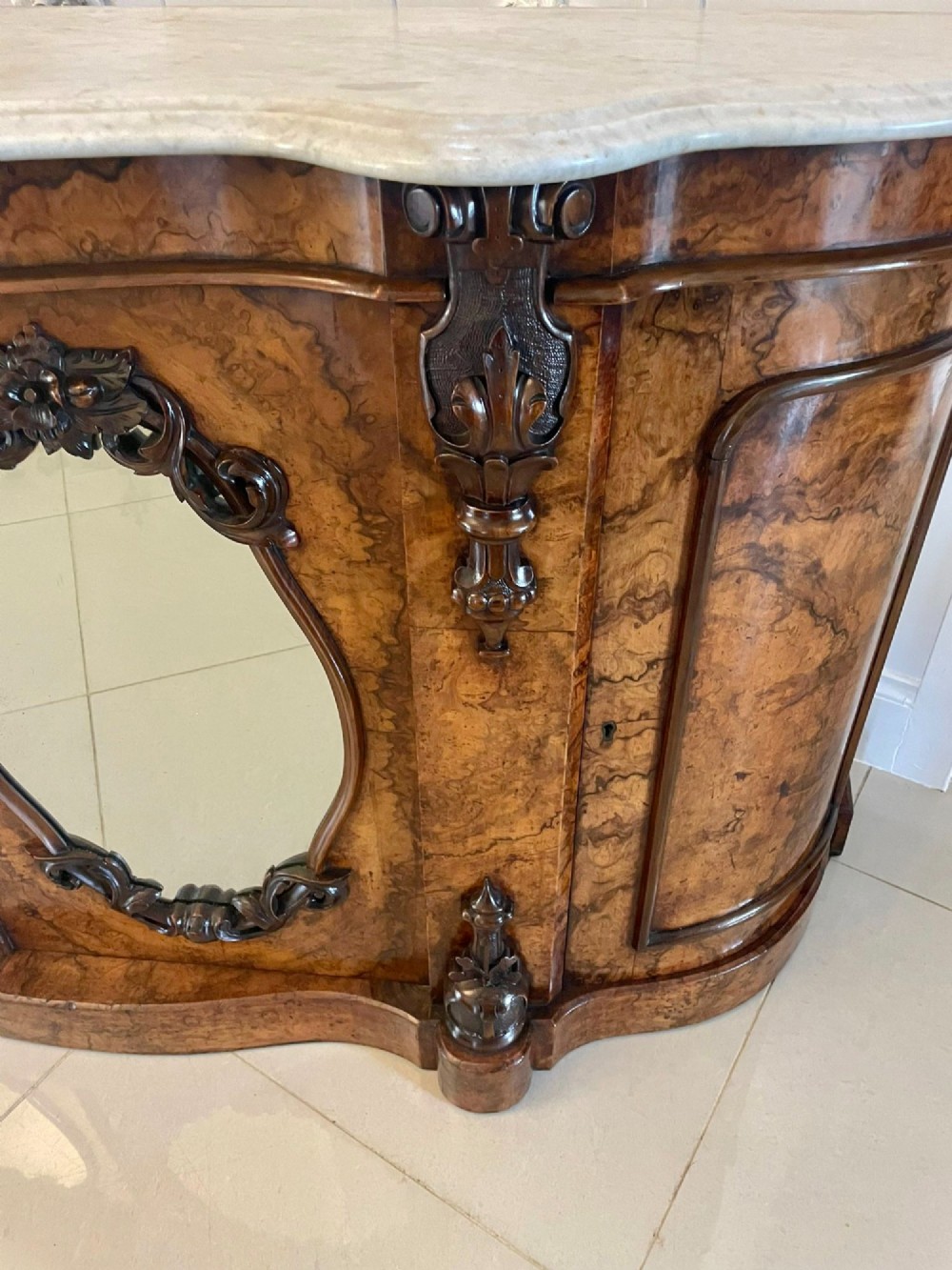 A Victorian burr walnut credenza featuring a serpentine white marble top, mirrored cupboard doors, and a large oval mirror back with carved scrolling detail. View XIII