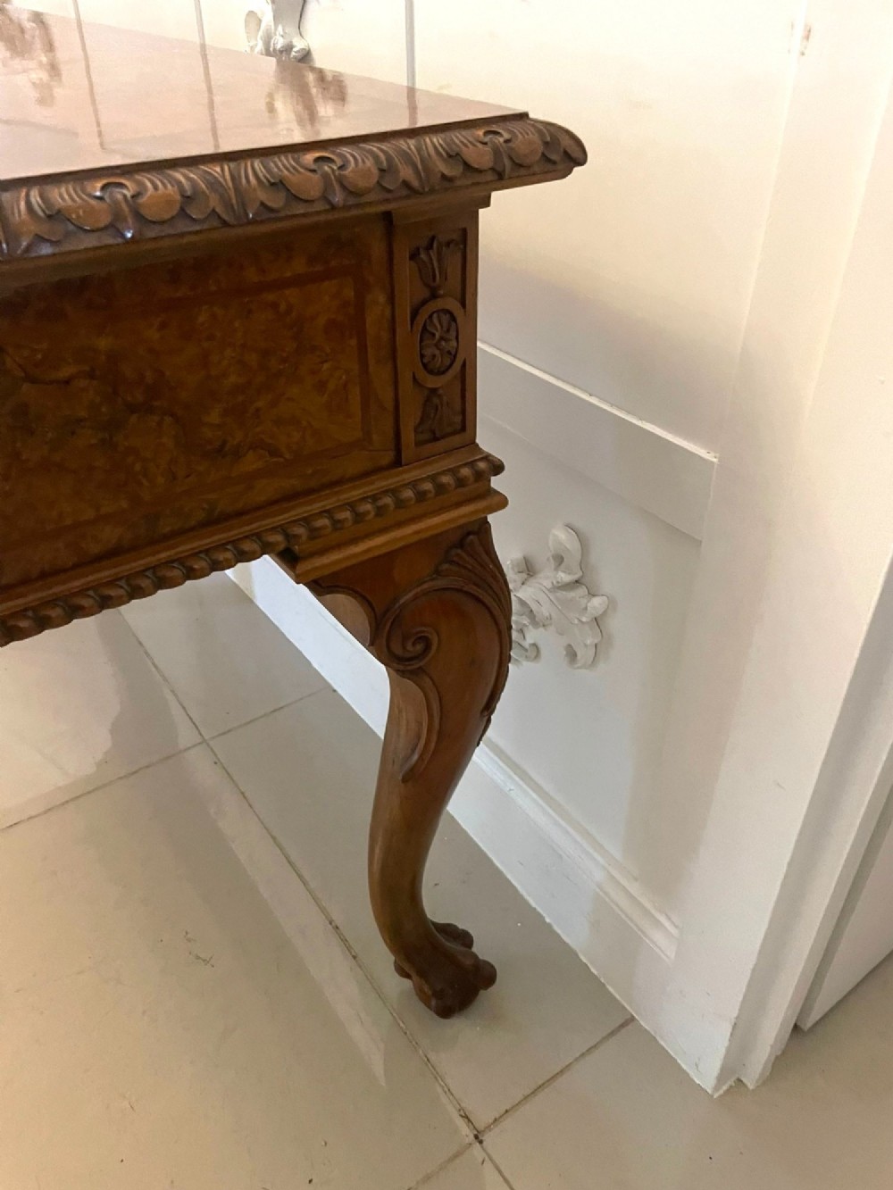An antique burr walnut console table featuring two drawers, intricate carved moulding along the frame, and carved cabriole legs ending in claw feet. View IX