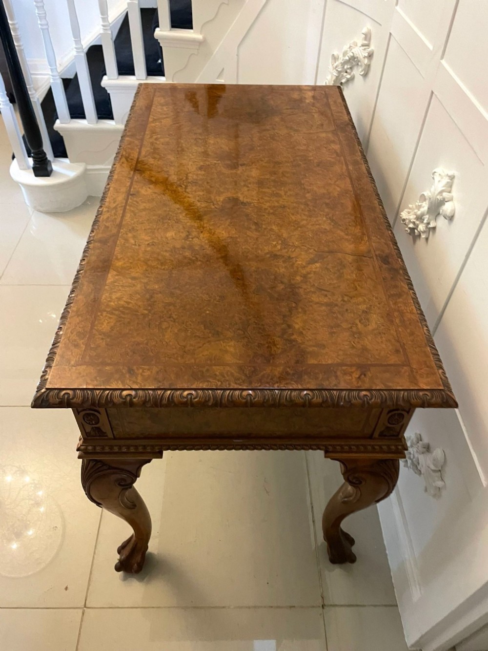 An antique burr walnut console table featuring two drawers, intricate carved moulding along the frame, and carved cabriole legs ending in claw feet. View X