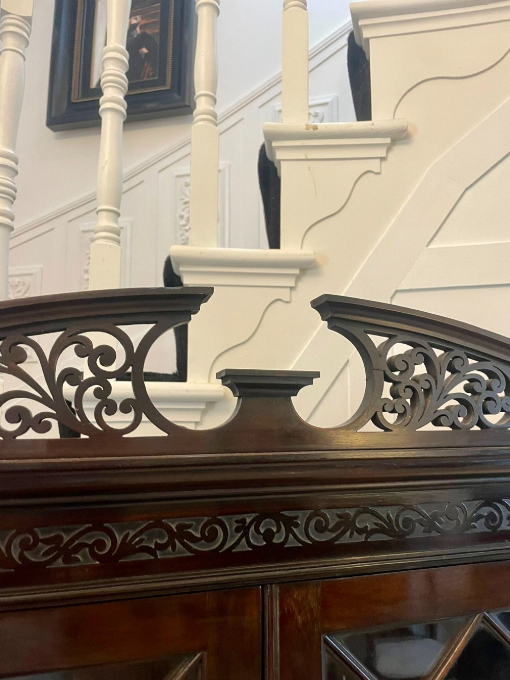 A dark carved mahogany display cabinet featuring astragal glazed doors, a pierced scrolled pediment, serpentine drawer fronts with brass handles, and a lower shelf. View VIII