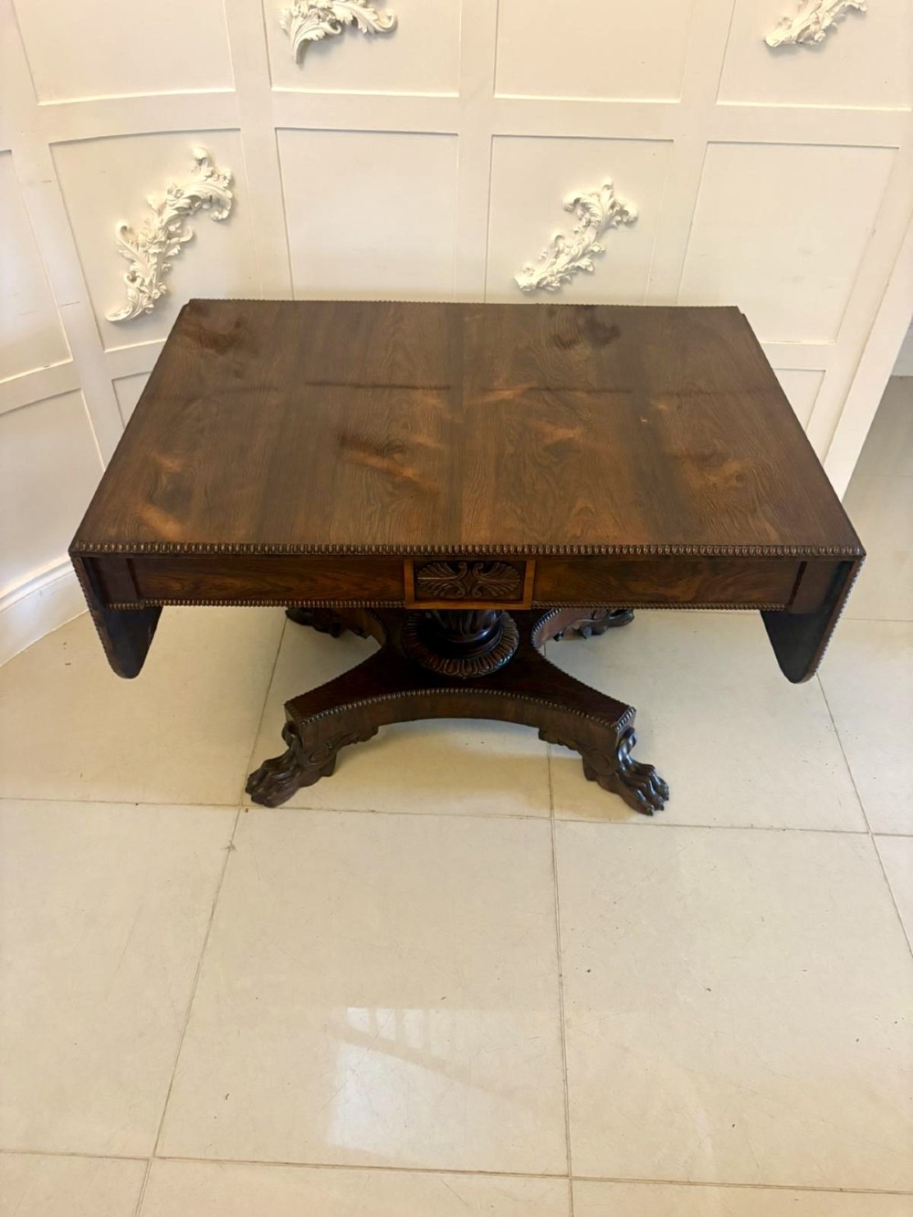 A Regency dark rosewood drop-leaf sofa table with a turned pedestal base and carved claw feet.